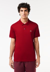 Rød bomulds polo shirt med krave, tre-knaps lukning, korte ærmer og lille grøn logo på venstre bryst.