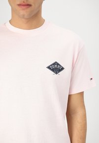 Camiseta de manga corta rosa claro hecha de algodón. Presenta un logo de diamante en navy en el lado izquierdo del pecho y un pequeño acento tricolor en la manga.