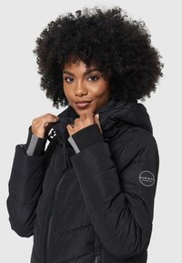 Black puffer jacket with a high collar and adjustable hood. Features elastic cuffs, quilted texture, and a side logo patch.
