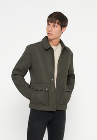 Donkergroene wolmix jacket met een kraag, drukknoopsluiting en twee frontzakken. Geplaatst op een effen witte achtergrond.