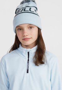Pull en polaire bleu clair avec un col haut et une fermeture éclair mi-hauteur. Assorti à un bonnet en tricot bleu clair avec un texte foncé et un pompon sur le dessus.