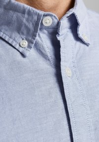 Ljusblå skjorta med knappar i ett texturerat tyg, med spridd krage och vita knappar, synlig sömnad och en tight passform.