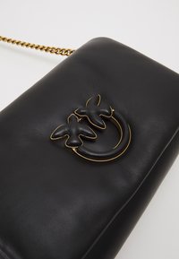 Borsa a tracolla in pelle nera con catena dorata e un motivo decorativo con due farfalle al centro, caratterizzata da superfici lisce e texture.