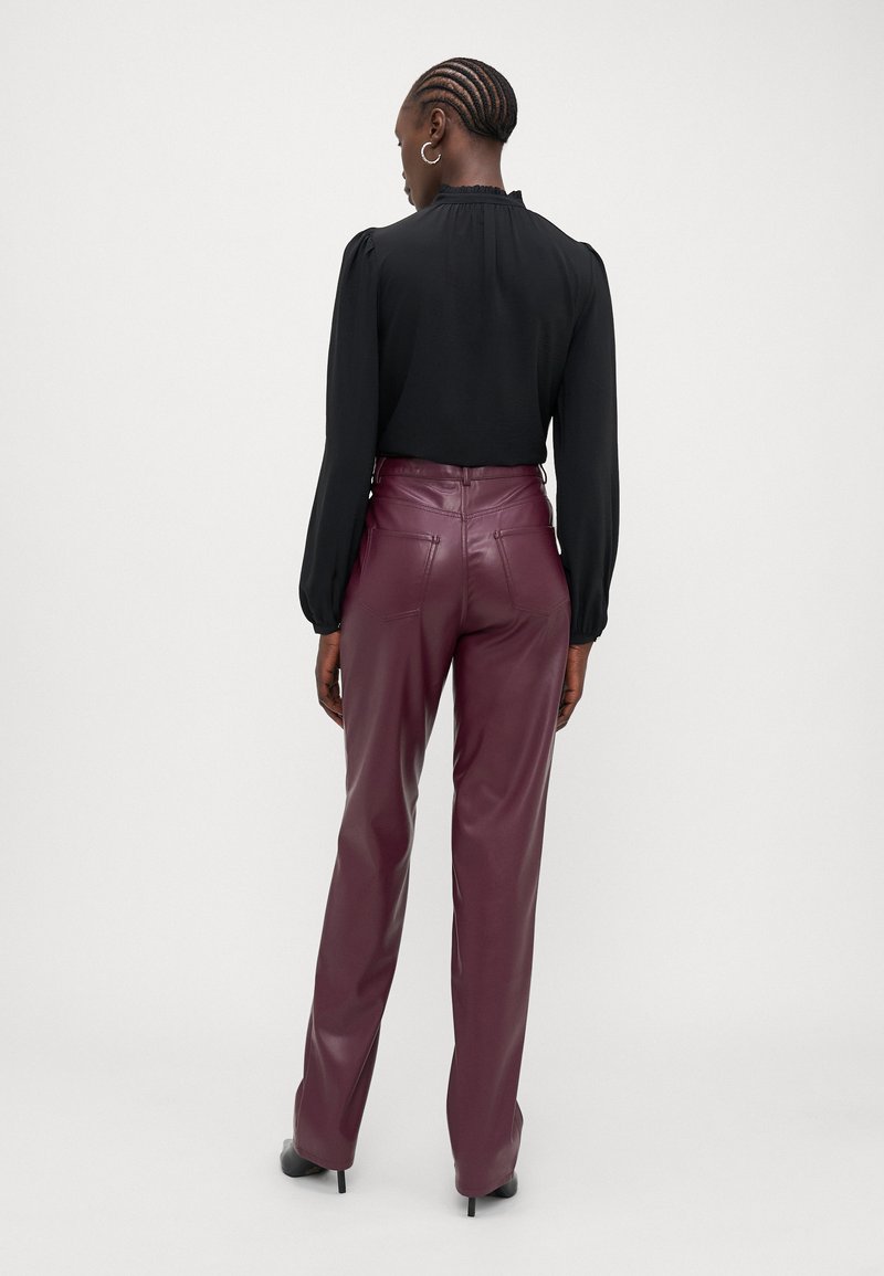 Blusa nera a maniche lunghe con scollo arricciato, abbinata a pantaloni in pelle bordeaux a vita alta con tasche posteriori e design a gamba dritta.