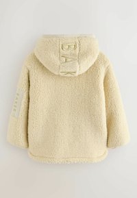 Kermaviininvärinen fleece-takki hupulla, jossa on brodeerattu "BAK" takana ja "BAKER" hihassa. Pehmeä rakenne, rento muotoilu.