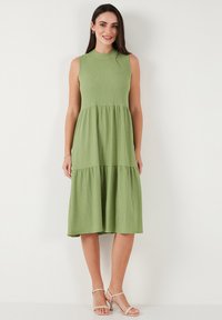 Green, sleeveless midi dress with a round neckline, tiered design, textured fabric, and a relaxed fit, paired with light sandals.