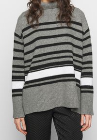 Szary i czarny sweter w paski z wysokim kołnierzem. Posiada grubą białą tasiemkę oraz ściągacz u dołu. Miękka dzianina o luźnym kroju.