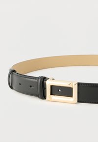 Μαύρη δερμάτινη ζώνη με ταμπά εσωτερική επένδυση και χρυσή ορθογώνια μεταλλική αγκράφα, απλωμένη σε λευκή επιφάνεια.