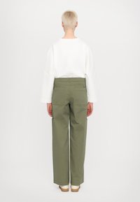 Haut long à manches blanches avec des poignets surdimensionnés, associé à un pantalon ample vert olive avec des poches latérales et un design de taille épurée.