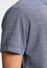 Kortärmad skjorta i ett strukturerat blått och vitt mönster, med en knappad krage och en snygg sömnad längs sömmarna.