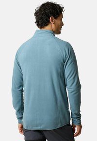 Pullover in pile blu chiaro con colletto, maniche lunghe e una texture liscia. Presenta cuciture piatte e un piccolo logo sul lato inferiore.