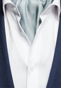 Vit skjorta med v-hals, prydd med en ljusblå satin scarf och en mörk marinblå jacka. Skjortan har knappstängningar och en slät yta.