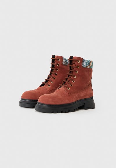 Brown suede boots with a black rubber sole, featuring gold eyelets and a multicolored patterned cuff. Ankle-height design with lace-up front.