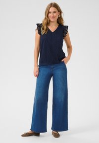 Haut bleu marine brodé avec des manches courtes en dentelle, associé à un pantalon en denim bleu à jambes larges et des chaussures plates marron.