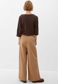 Bruine, losse top met wijde halslijn; tan, high-waist, brede broekspijpen met twee achterzakken; textiel met een structuur; enkel-lengte.