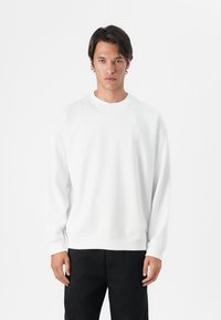 Sweatshirt branco de gola redonda feito de algodão, com mangas longas, punhos canelados e um corte descontraído. Sem logótipos ou padrões visíveis.