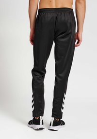 Zwarte sportbroek met een gladde textuur, voorzien van witte streepaccenten langs de zijkanten en ritsen bij de enkelboorden. Elastische tailleband.