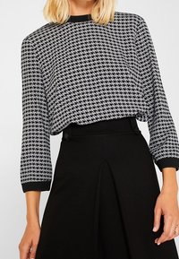 Schwarz-weißer Hahnentrittmuster-Oberteil mit lockerer Passform, rundem Halsauschnitt und Dreiviertelärmeln. Gerippte schwarze Säume und Saum.
