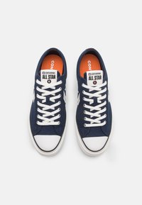 Marina canvas sneakers med vita snören och gummisula, med en vit tåhuvud och orange innersula med "Converse All Star" branding.