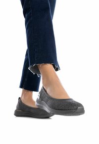 Zapatos gris sin cordones con parte superior de punto texturizado y suela flexible. Combinados con jeans de mezclilla oscura que presentan dobladillos deshilachados.