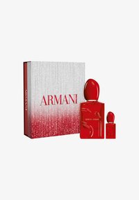 Røde parfumeflasker med runde kapsler er udstillet ved siden af en glansfuld hvid og rød æske med glitrede accenter og fed "ARMANI" tekst.