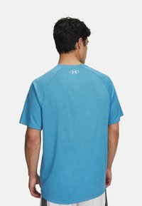 Camiseta deportiva de color azul claro con mangas cortas, tejido texturizado, cuello redondo y un pequeño logo en la parte posterior cerca del cuello.