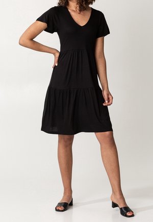 Musta kerroksittain laskeutuva mekko kevyestä kankaasta, jossa syvä V-pääntie ja lyhyet hihat. Mekolla on rento istuvuus ja levenevä siluetti.