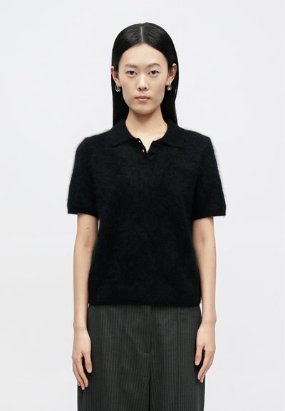 Sort kortærmet polo-trøje lavet af blødt materiale med krave og tre knapper. Kombineret med mørke bukser med tynde striber.