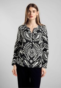 Blusa a maniche lunghe bianco e nero con colletto abbottonato e motivo paisley. Tessuto leggero con una texture liscia e orlo curvo.