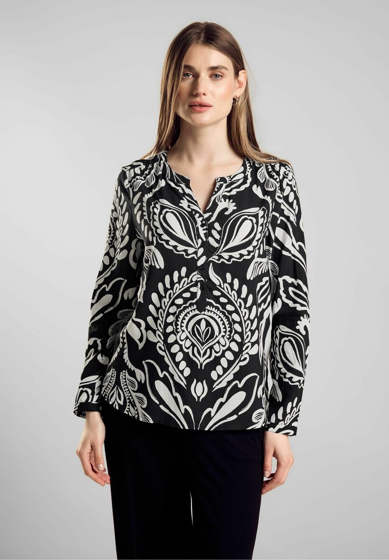 Blusa a maniche lunghe bianco e nero con colletto abbottonato e motivo paisley. Tessuto leggero con una texture liscia e orlo curvo.