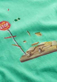 Tessuto verde menta con una grafica stampata raffigurante un segnale di stop, scarpe da ginnastica e forme galleggianti, con accenti rossi e gialli.