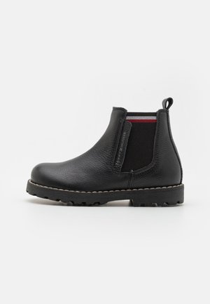 Stivaletto Chelsea in pelle nera con pannelli elastici laterali, tomaia testurizzata, linguetta e strisce decorative rosse e bianche a contrasto. Suola in gomma.