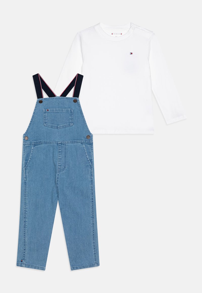 Denim overalls with adjustable navy straps, featuring two front pockets and a back pocket, paired with a long-sleeve white shirt.