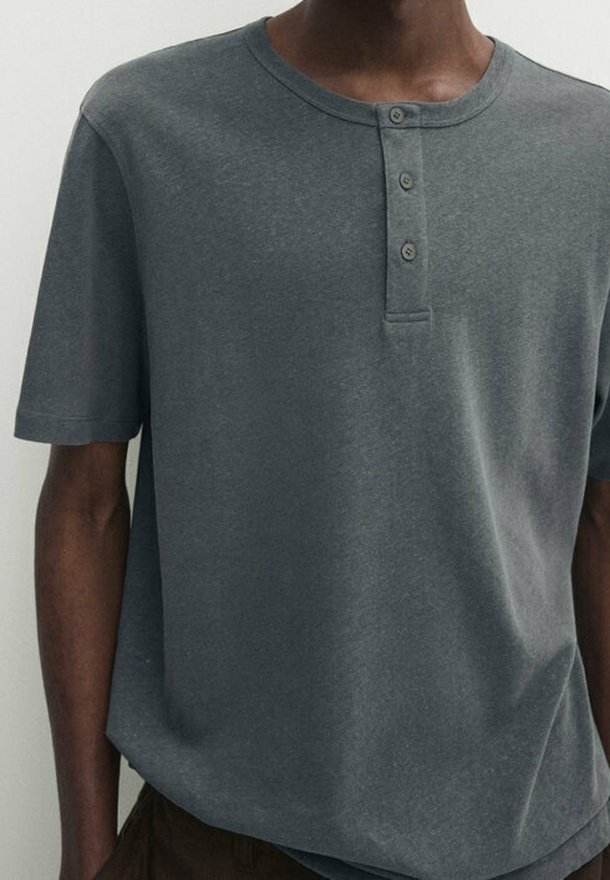 Homme portant un t-shirt henley à manches courtes gris foncé avec trois boutons sur le plastron avant.