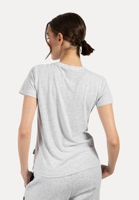 Camiseta gris de manga corta hecha de una tela suave y lisa. Presenta un corte relajado y un escote sencillo, con una etiqueta visible en el dobladillo.