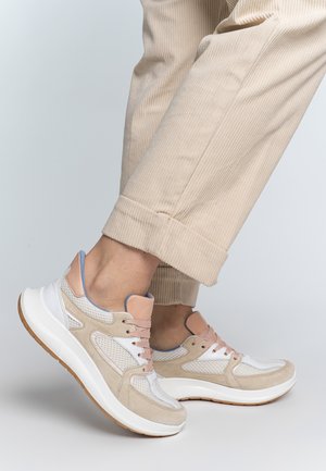 Beige sneaker with mesh and suede material, white accents, pink laces, and a rounded white sole. Close-up view with ribbed pants.