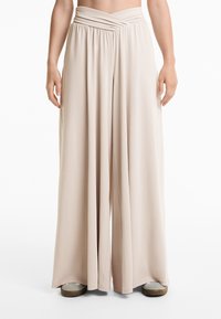 Beige weit geschnittene Hosen mit einem gerafften Taillenbund, aus einem weichen, dehnbaren Stoff, mit einem fließenden Design und einer glatten Textur.