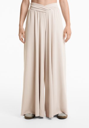 Beige wide-leg pants with a ruched waistband, made from a soft, stretchy fabric, featuring a flowing design and a smooth texture.