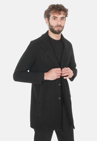 Cappotto di lana nero con rever a scollo a V, design a un petto e sei bottoni, dotato di tasche laterali e una superficie liscia.