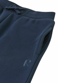 Granatowe dresy wykonane z miękkiego materiału, z prążkowanym paskiem w talii oraz sznurkiem do regulacji i bocznymi kieszeniami. Subtelny detal logo na nodze.