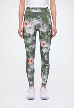 Modèle portant un legging vert taille haute à imprimé floral flou, un haut blanc et des baskets blanches.