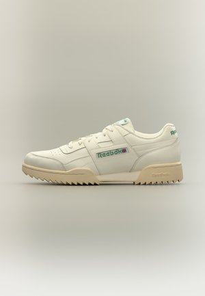 Weißer Reebok Sneaker mit grünem Logo, beiger Sohle, Schnürdesign und Zickzack-Profil, seitlich auf neutralem Hintergrund gezeigt.