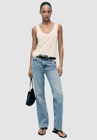 Outfit casual composto da un top a canotta aderente color crema, jeans dritti blu chiaro, cintura nera e borsa nera. Sandali piatti completano il look.