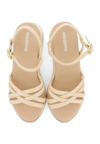 Beige sandals with cross-over straps and a buckle closure. Made of synthetic material, featuring a flat sole and smooth texture.