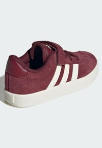 Burgundska suede tenisica s bijelim trostrukim dizajnom, podstavljenim ogradom i teksturiranim izgledom, s ravnim bijelim gumenim potplatom.