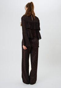 Yksivärinen leopardi-tyylinen asukokonaisuus, joka sisältää kerroksittain laskeutuvan paitapuseron, jossa on liehuvat hihat, sekä leveät housut, valmistettu kevyestä kankaasta.