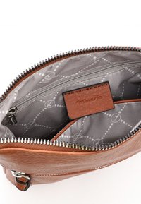 Der Innenraum der braunen synthetischen Lederhandtasche verfügt über ein grau gemustertes Futter, eine Zippertasche und ein braunes Etikett. Runde Muster sind sichtbar.