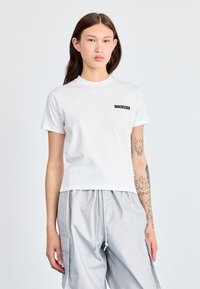 Balta medvilninė marškinėliai su apykakle ir trumpomis rankovėmis. Kairėje krūtinės pusėje yra juodas "DICKIES" logotipas. Modelis vilki pilkas kargo kelnes.