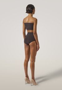 Svart bandeau-topp som matchas med högmidjade svarta trosor. Modellen bär nakna högklackade skor. Slätt tyg, minimalistisk design och sömlös silhuett.