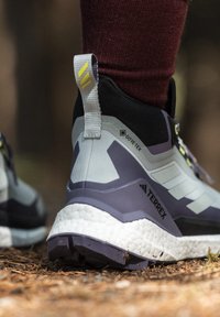 Scarpe da trekking GORE-TEX con un design rinforzato in grigio e viola, suola texturizzata e una distintiva intersuola bianca con accenti di branding.